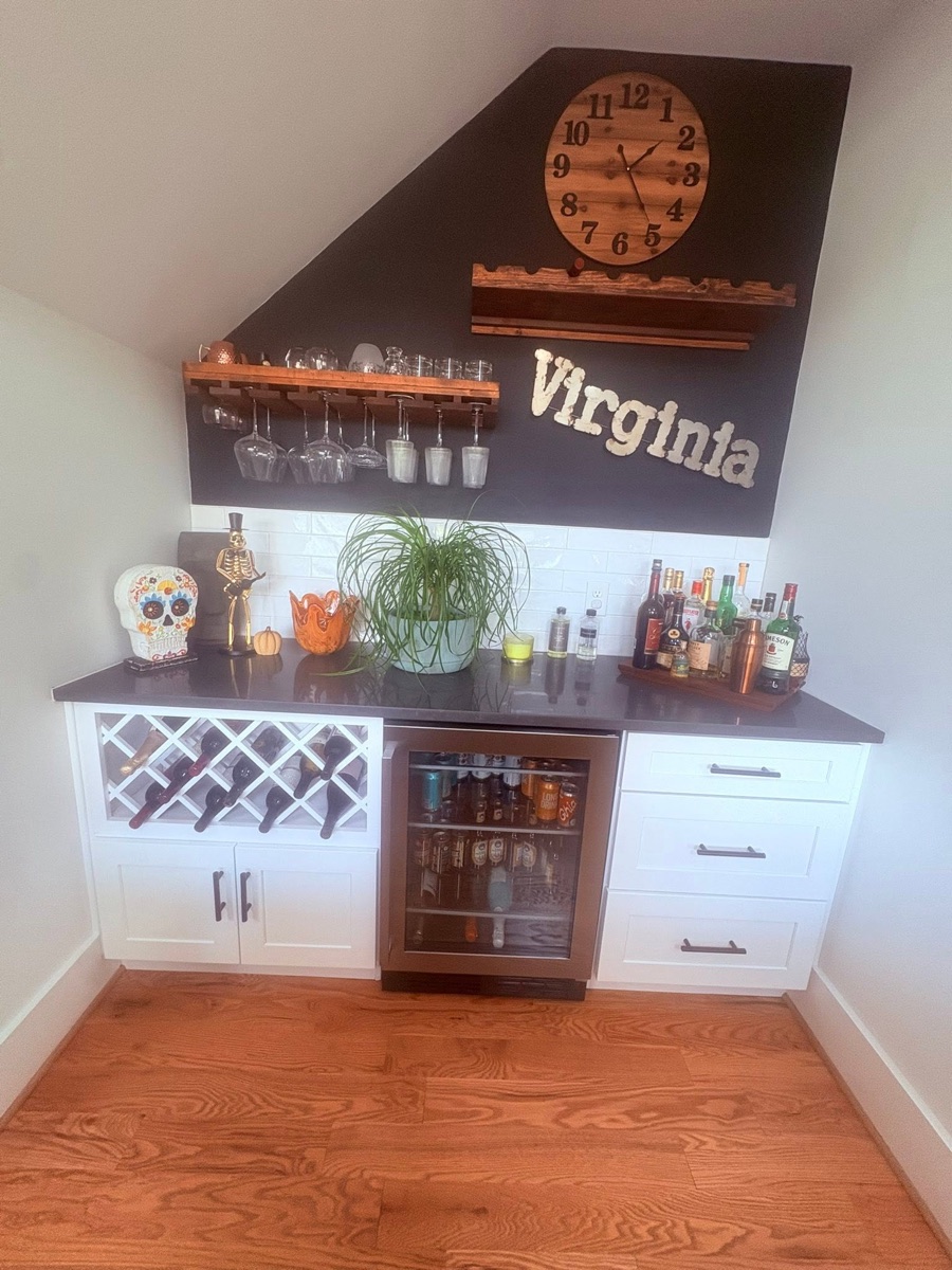 A clean home bar nook with a white tile backsplash, dark countertop, white cabinets and hardwood floor